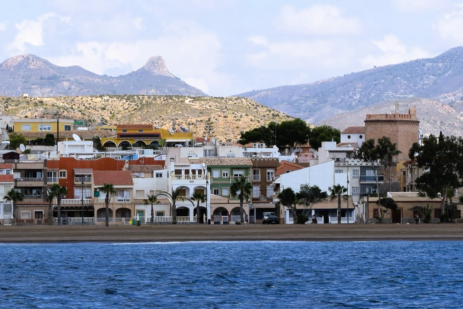 The colourful seafront of Bolnuevo viewed from the sea, with the old watchtower and mountains behind