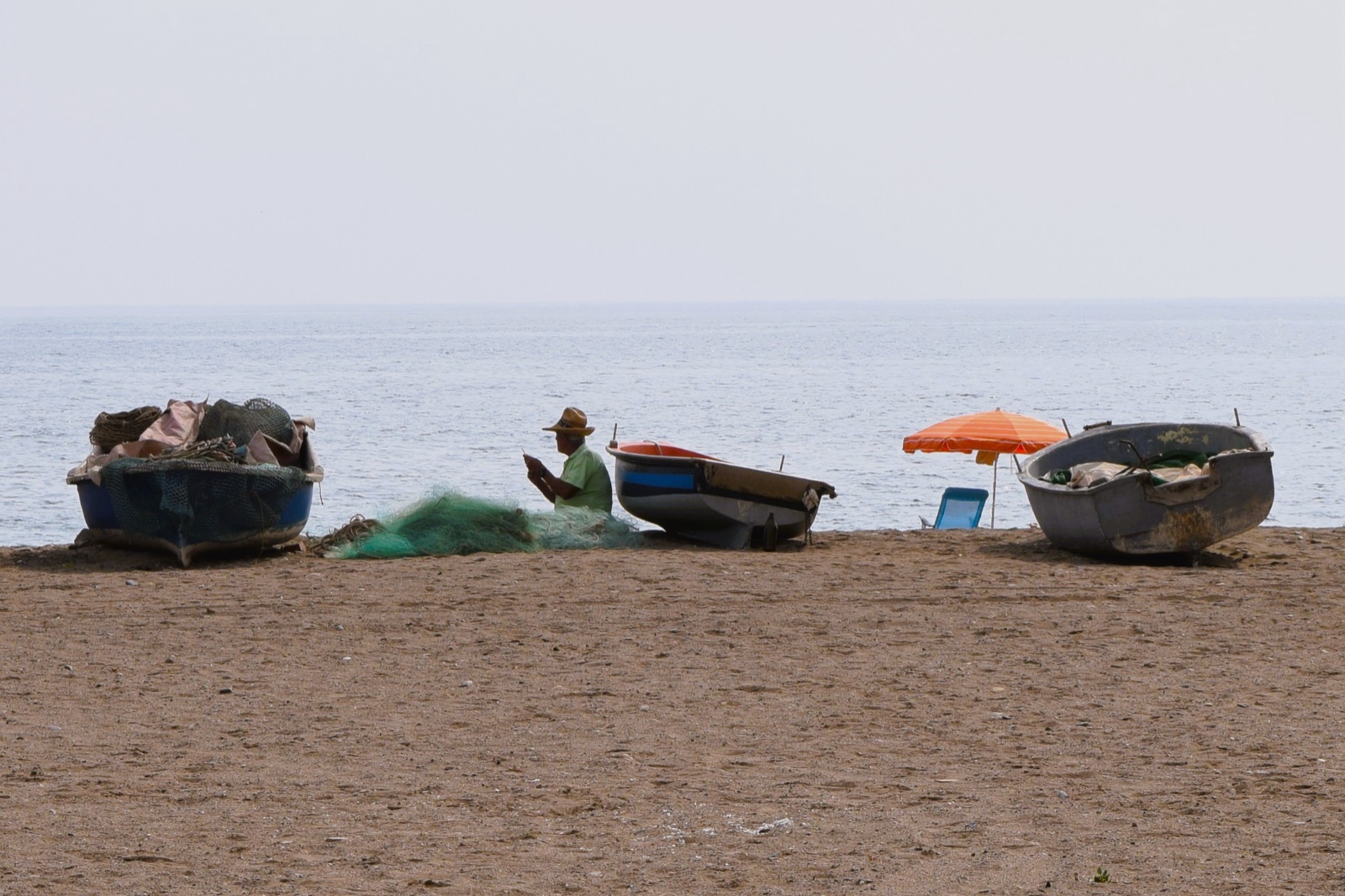A fisherman mending green nets between traditional boats on Bolnuevo beach