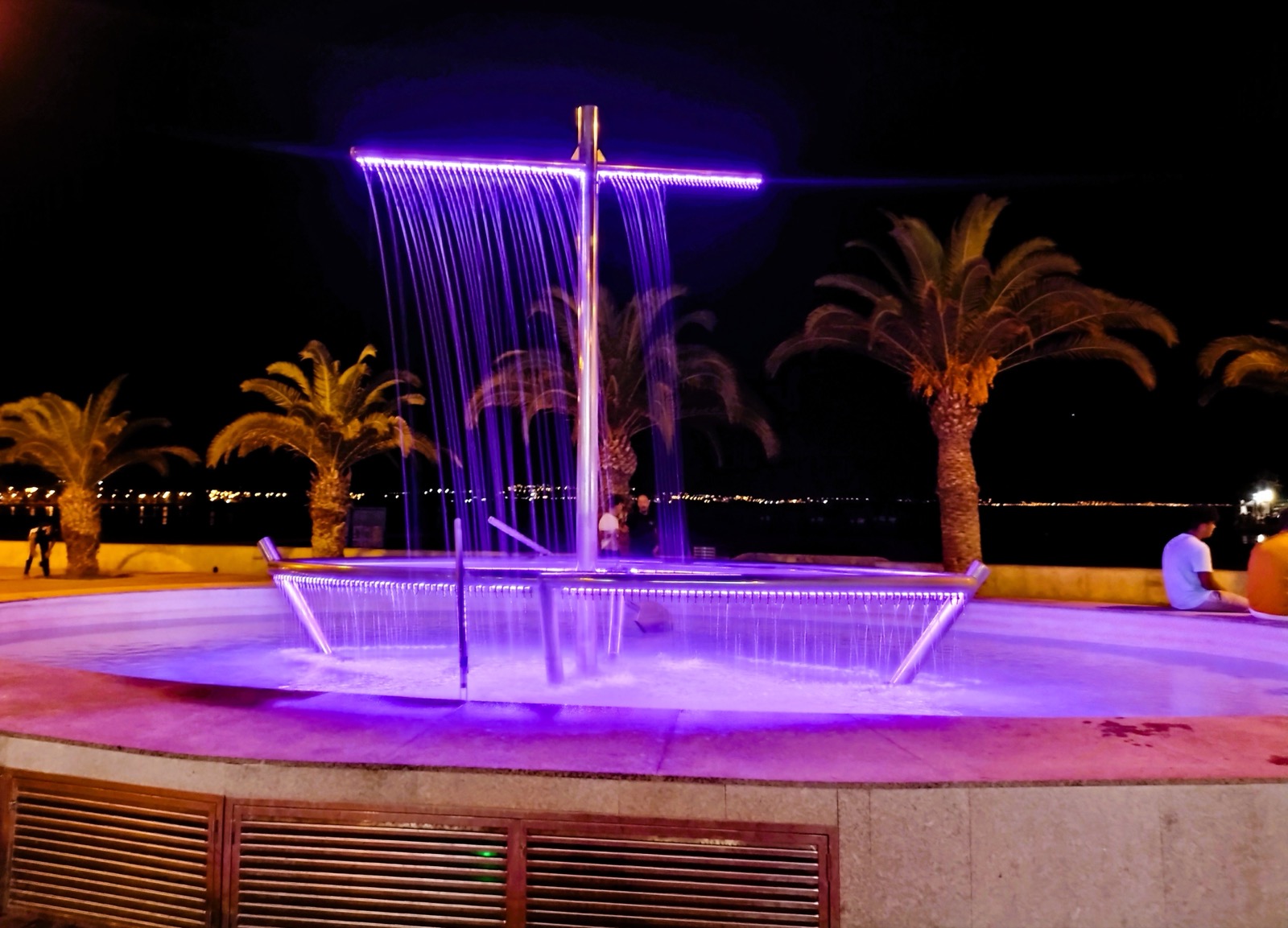 The illuminated boat-shaped fountain on the Puerto de Mazarrón seafront at night, lit purple