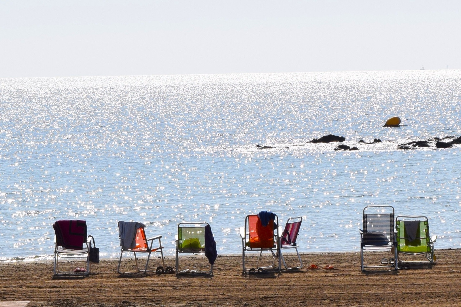 A row of colourful beach chairs facing the sparkling sea at Playa del Rihuete
