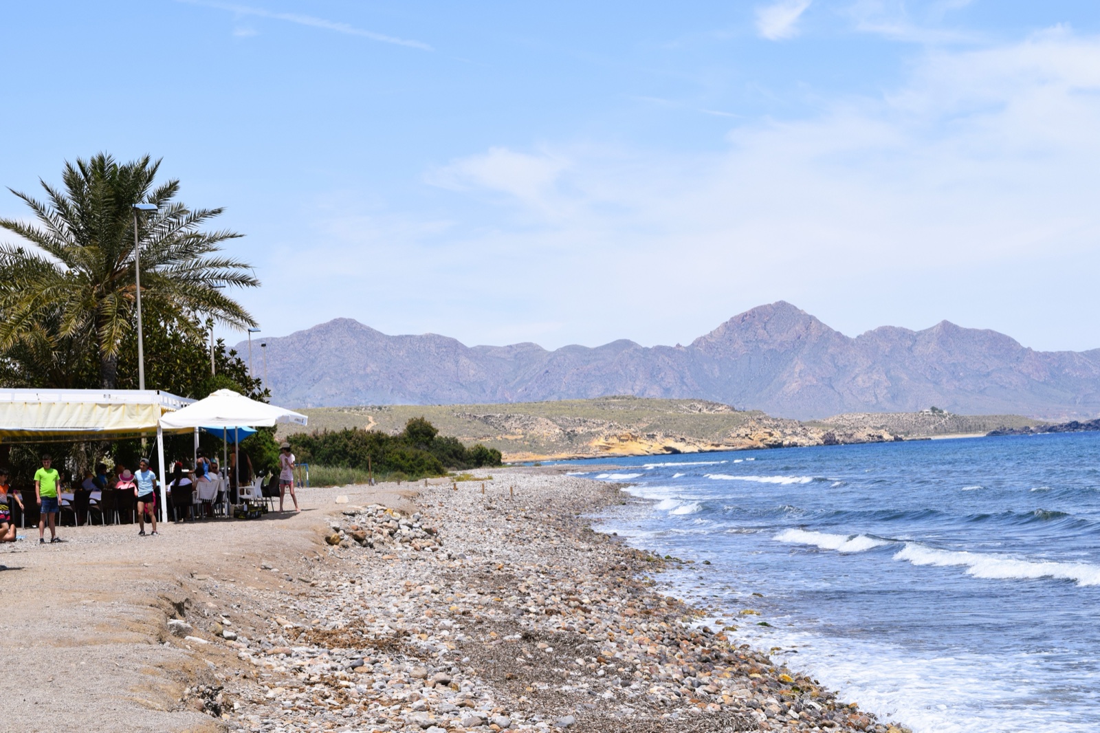 A beach restaurant under palm shade at Puntas de Calnegre with mountains behind