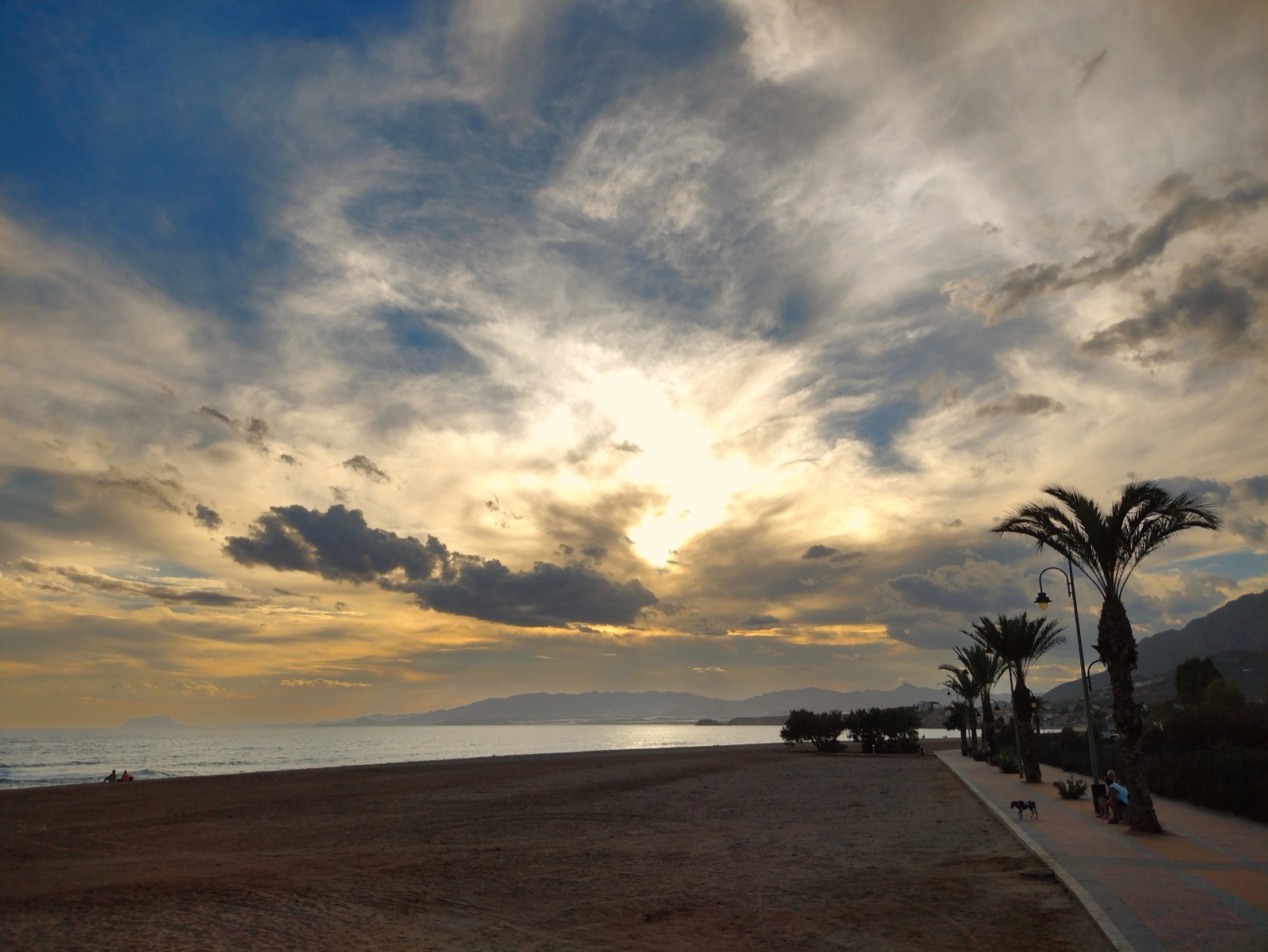 Golden sunset over Bolnuevo beach with palms and promenade